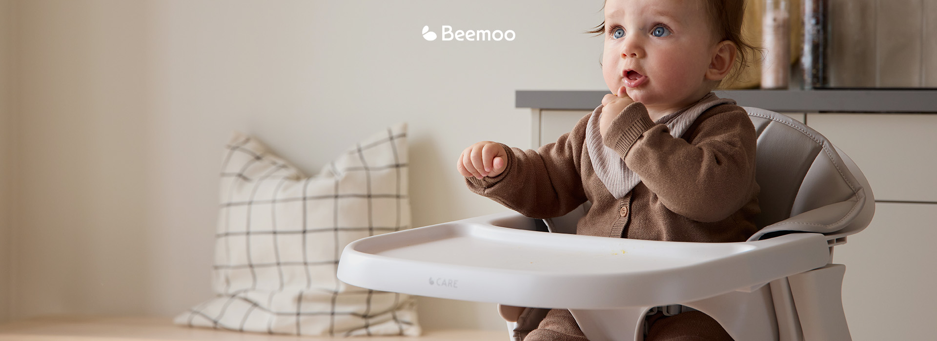 Barn sitter i en hög stol med texten 'Beemoo'.