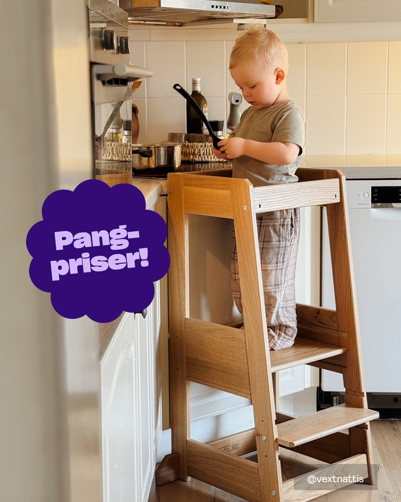 Pang-priser! En blond pojke står i ett kök på en barnpall, håller i köksredskap, omgiven av köksbänkar och en diskmaskin.