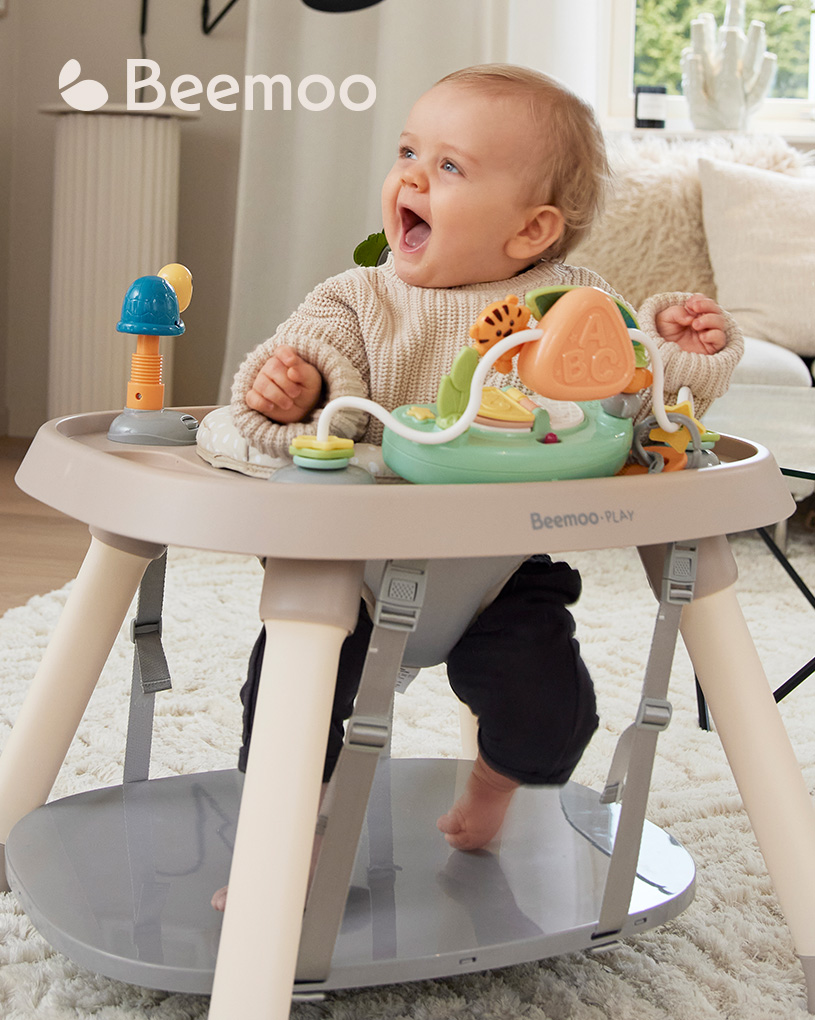 Bebis i rund lekstol med leksaker, leende och glad.