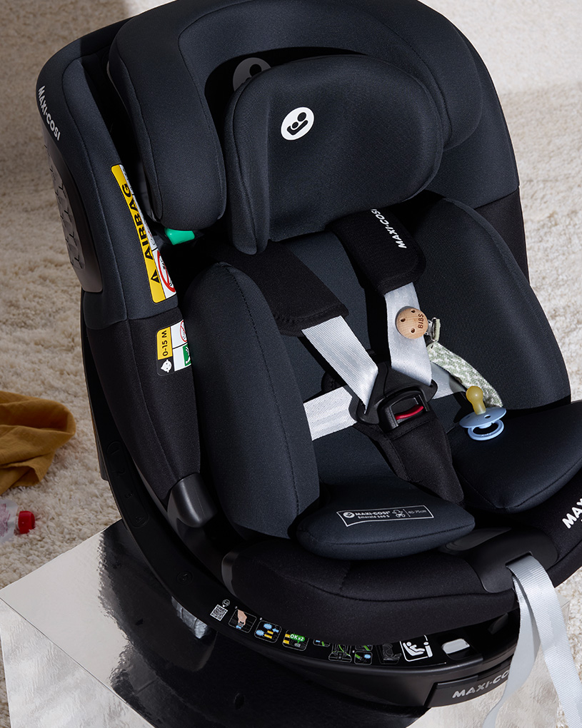 Svart bilbarnstol med säkerhetsanvisningar och en napp i botten.