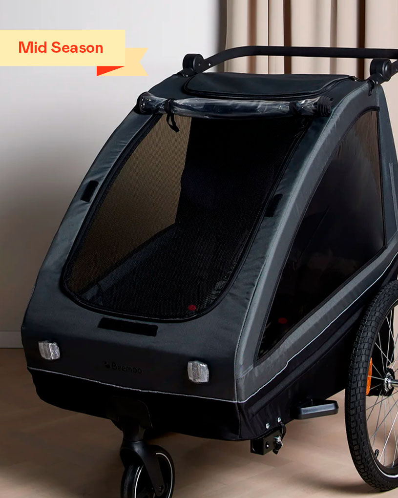 Svart barnvagn/transportvagn på hjul, studio. Etikett: “Mid Season”.