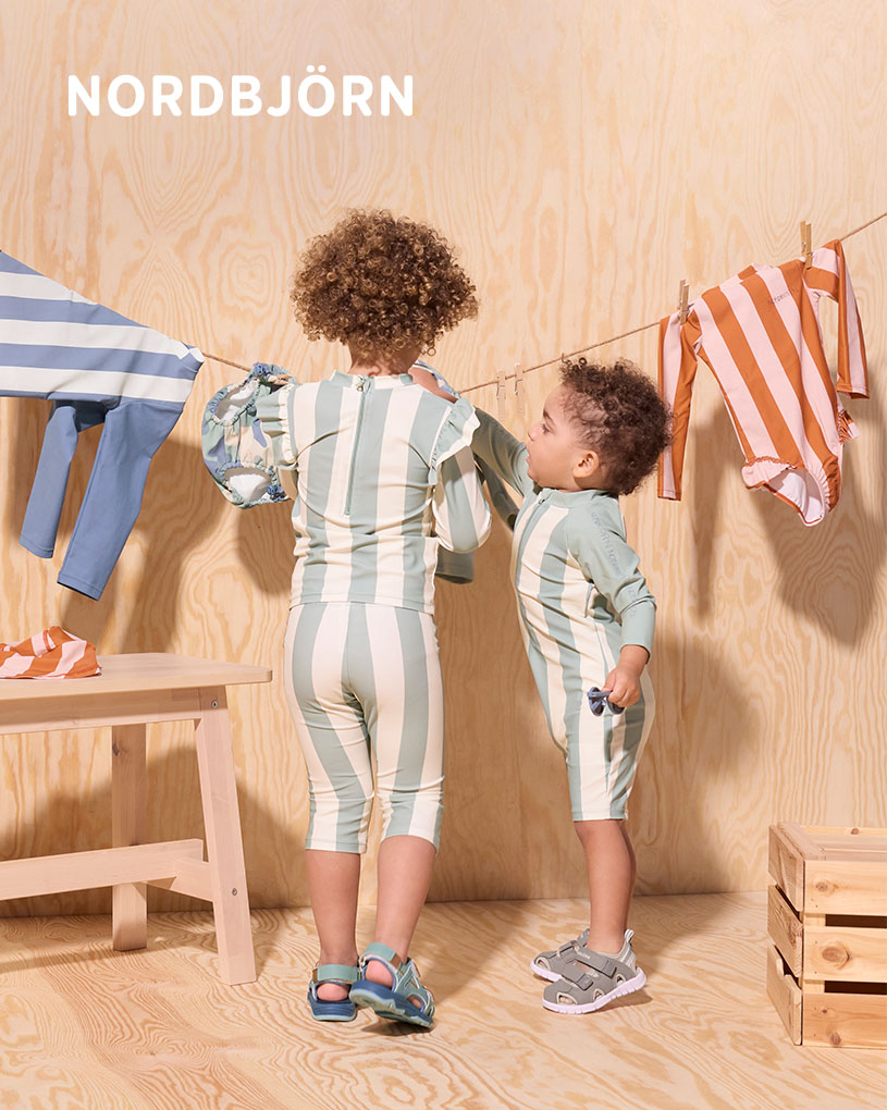 Barn i solhatt leker med hinkar på en trätrall.