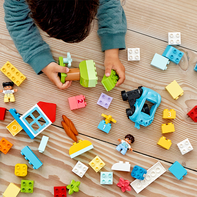 Barn leker med LEGO-klossar och en grön träfigur, med texten 'Byggsatser'.