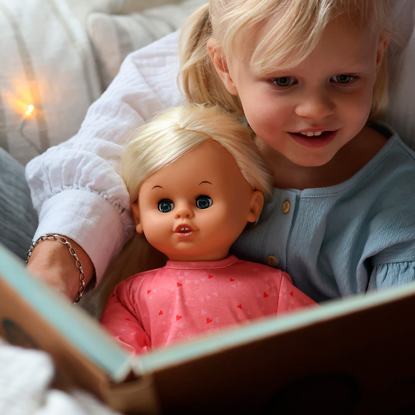 Liten flicka lägger en bebis i en vit spjälsäng.